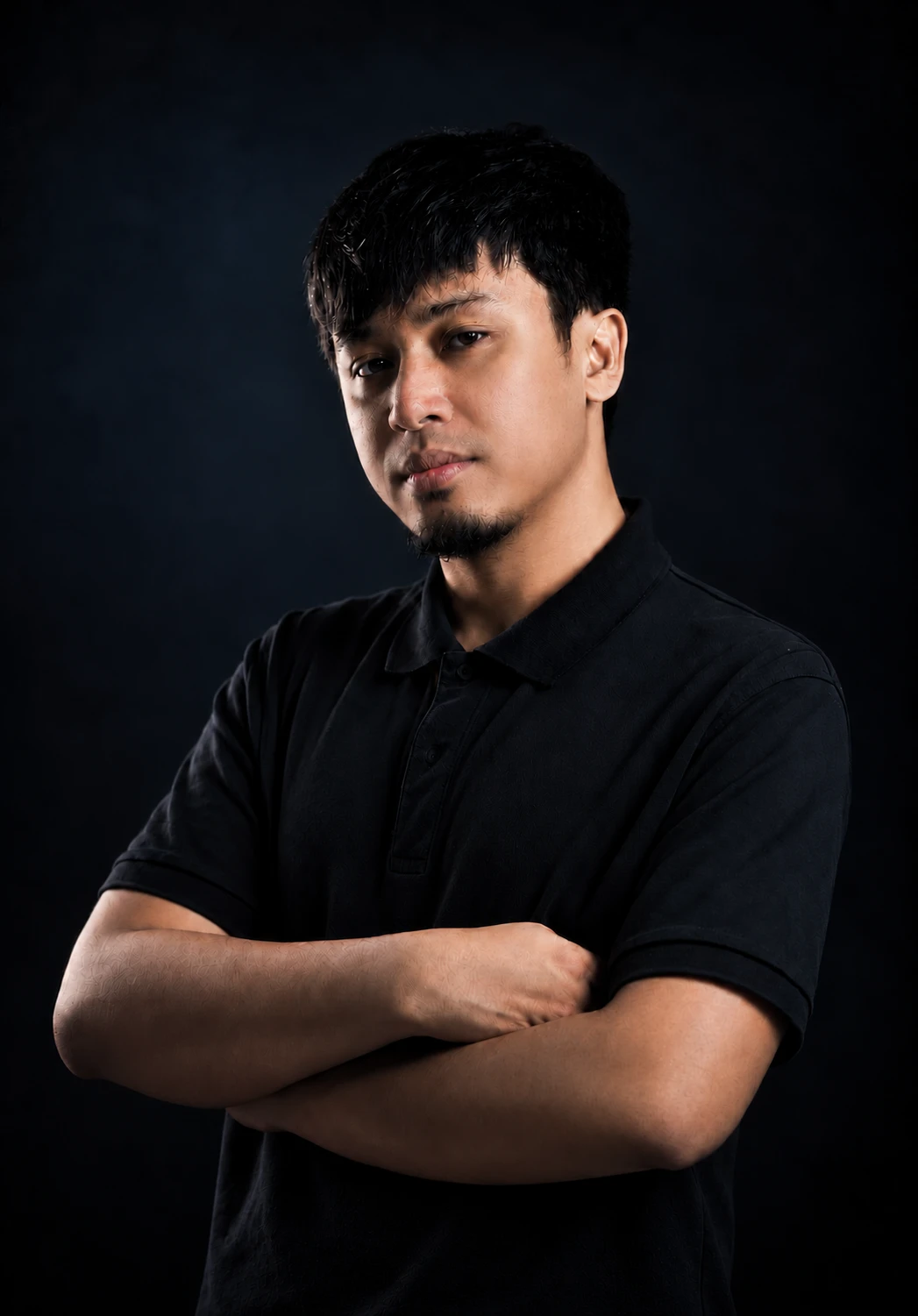 Angelo Aquino in a black polo shirt, arms crossed, against a dark background