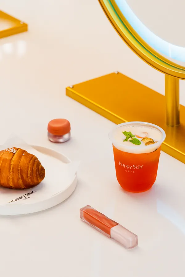 Croissant, iced drink and lip gloss on a white table