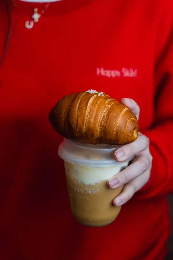 Hand holding a croissant on top of a drink