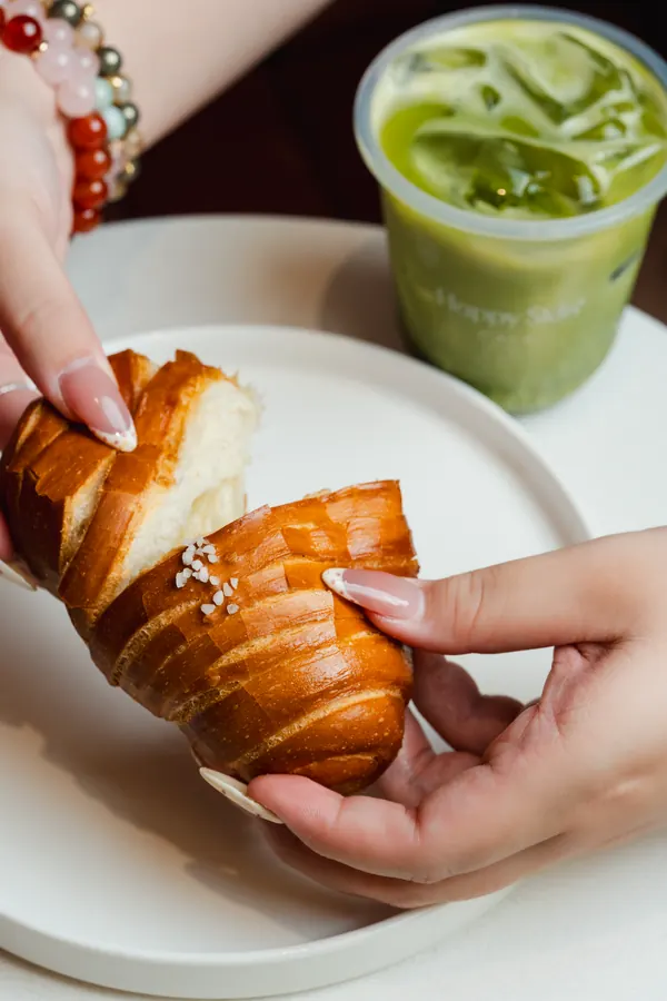 Hands tearing a croissant beside an iced matcha