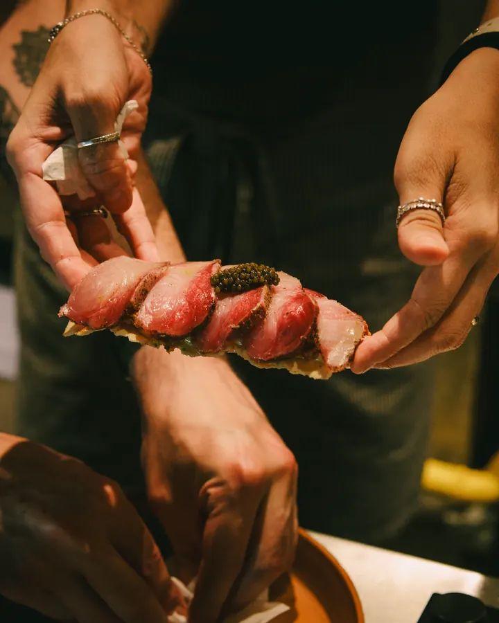 Hands holding a skewer of seared meat