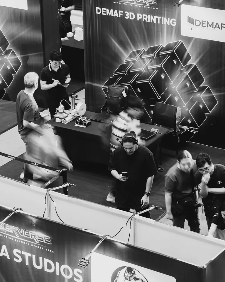 Visitors at a 3D printing booth, in black and white
