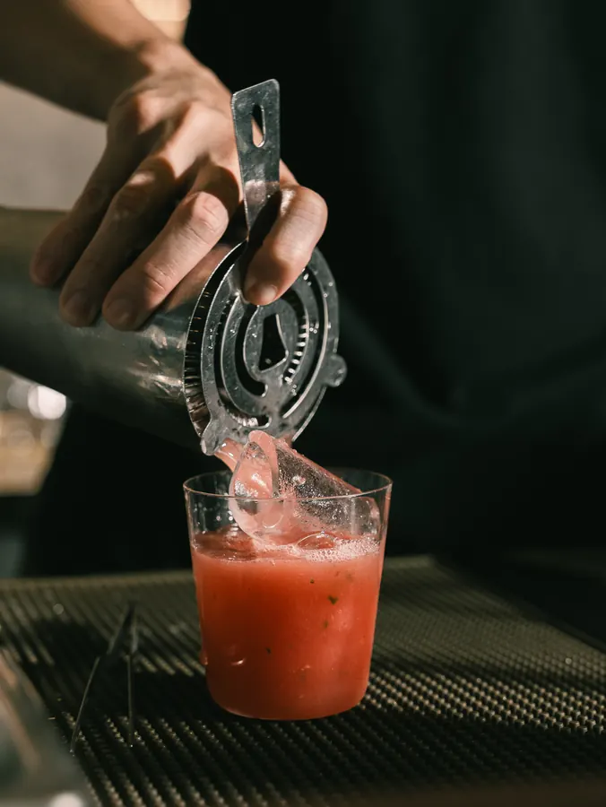 Straining a red drink over ice