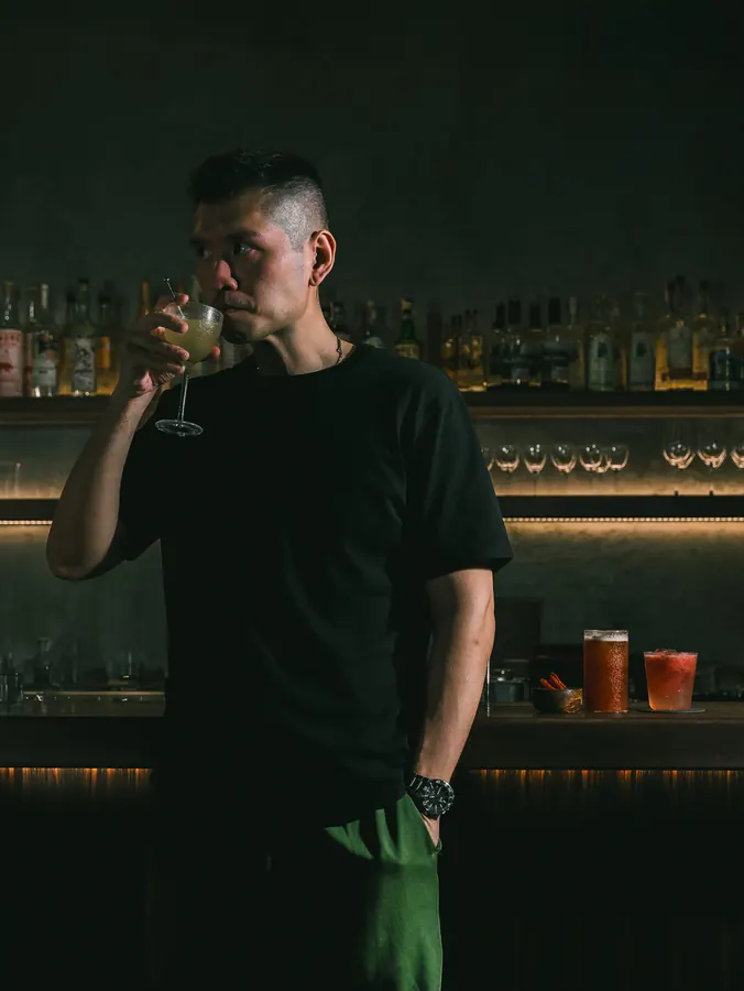 Royce Pua standing behind the bar with a drink